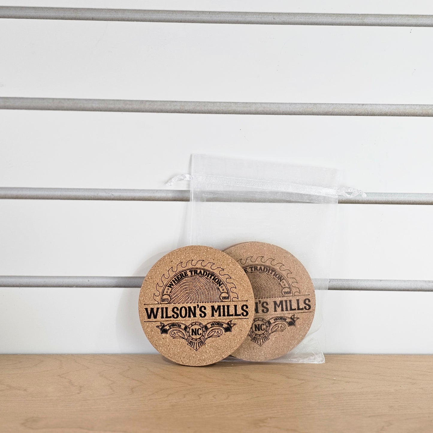Two round cork coasters with 'Wilson's Mills' branding on a wooden surface.