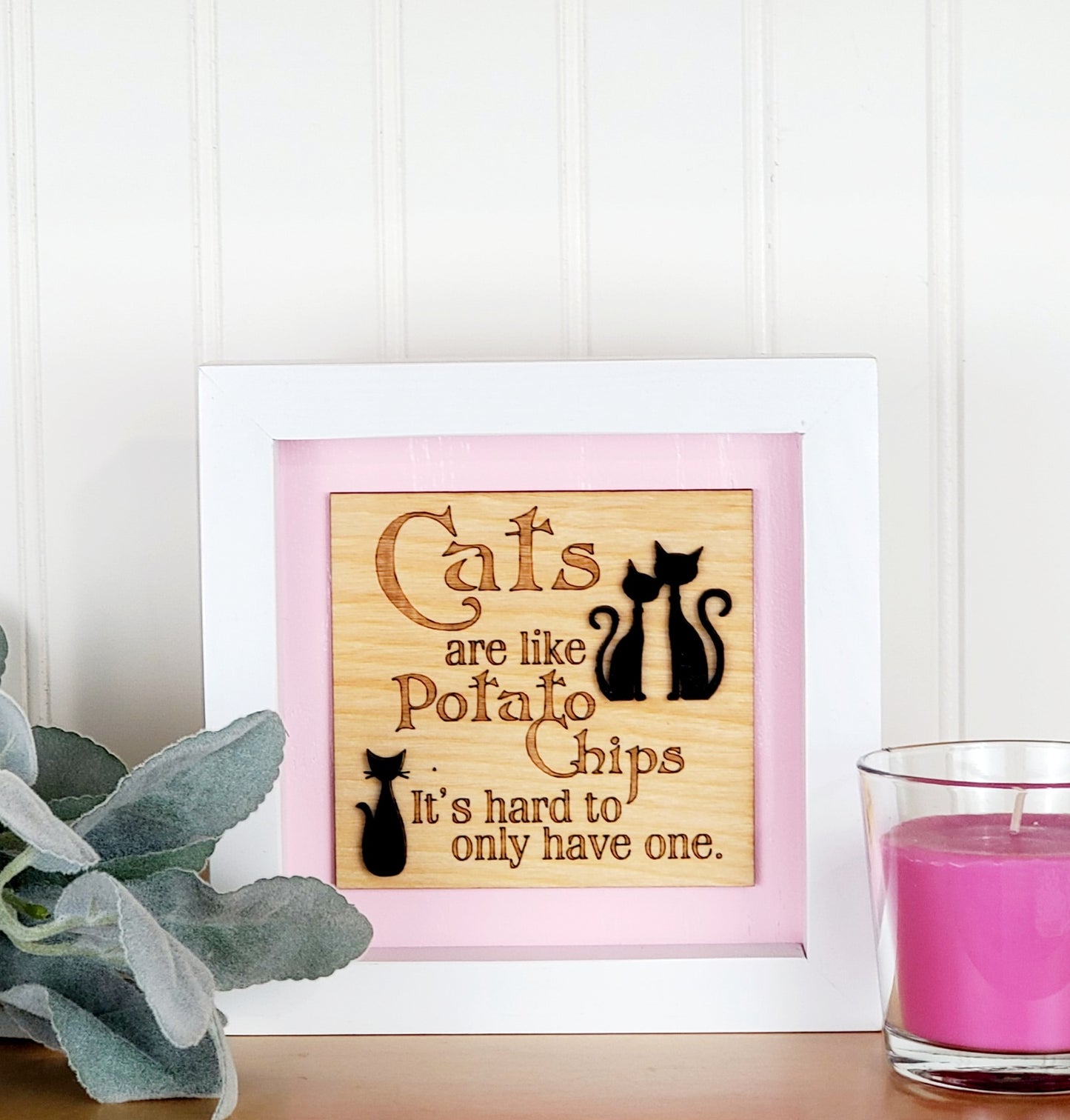 Cats are like potato chips, Its hard to have only one, engraved on natural birch wood cut out in the shape in a square and placed on your choice of baby pink or white background. White wood frame. Black mid century modern cats attached in a 3D manner. Aproximately, Six inch square tabletop sign.