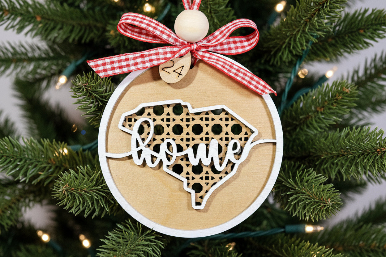 Wooden South Carolina ornament with 'home' cutout and red ribbon, surrounded by greenery