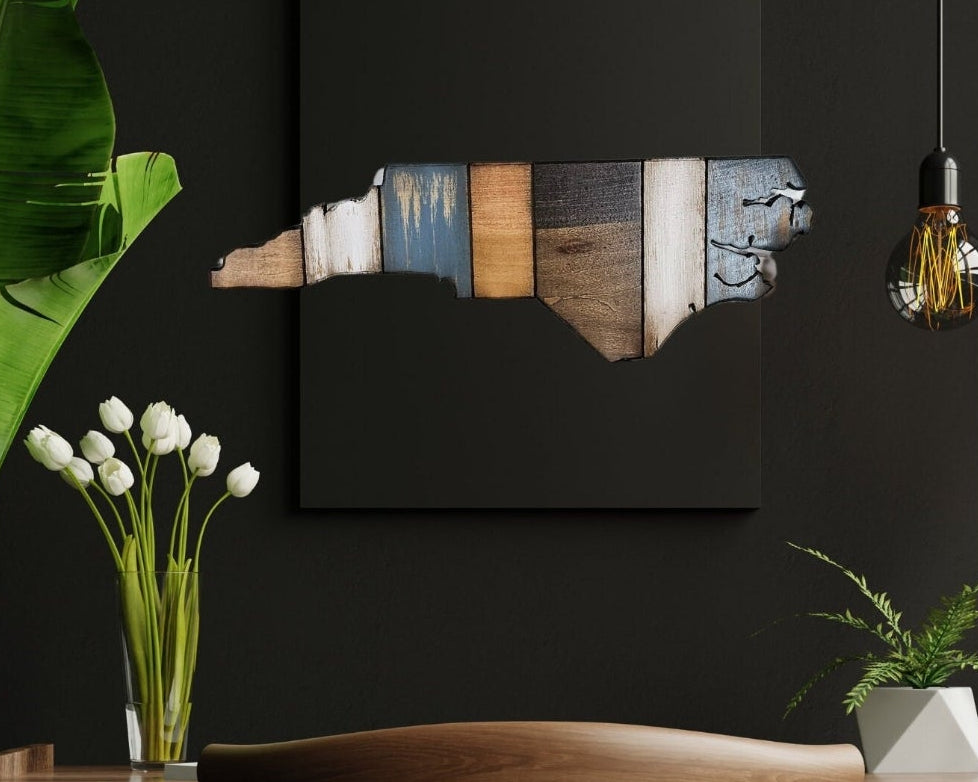 Decorative wall art with a North Carolina shape cutout on a dark wall, surrounded by plants and a vase.