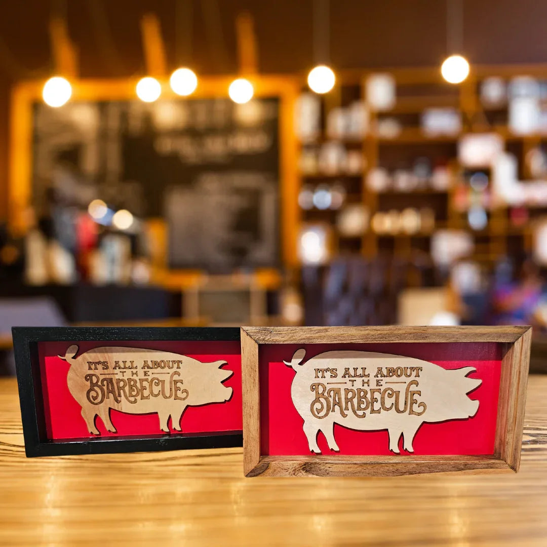 Two wooden pig signs with barbecue-themed designs on a blurred bar or restaurant background.