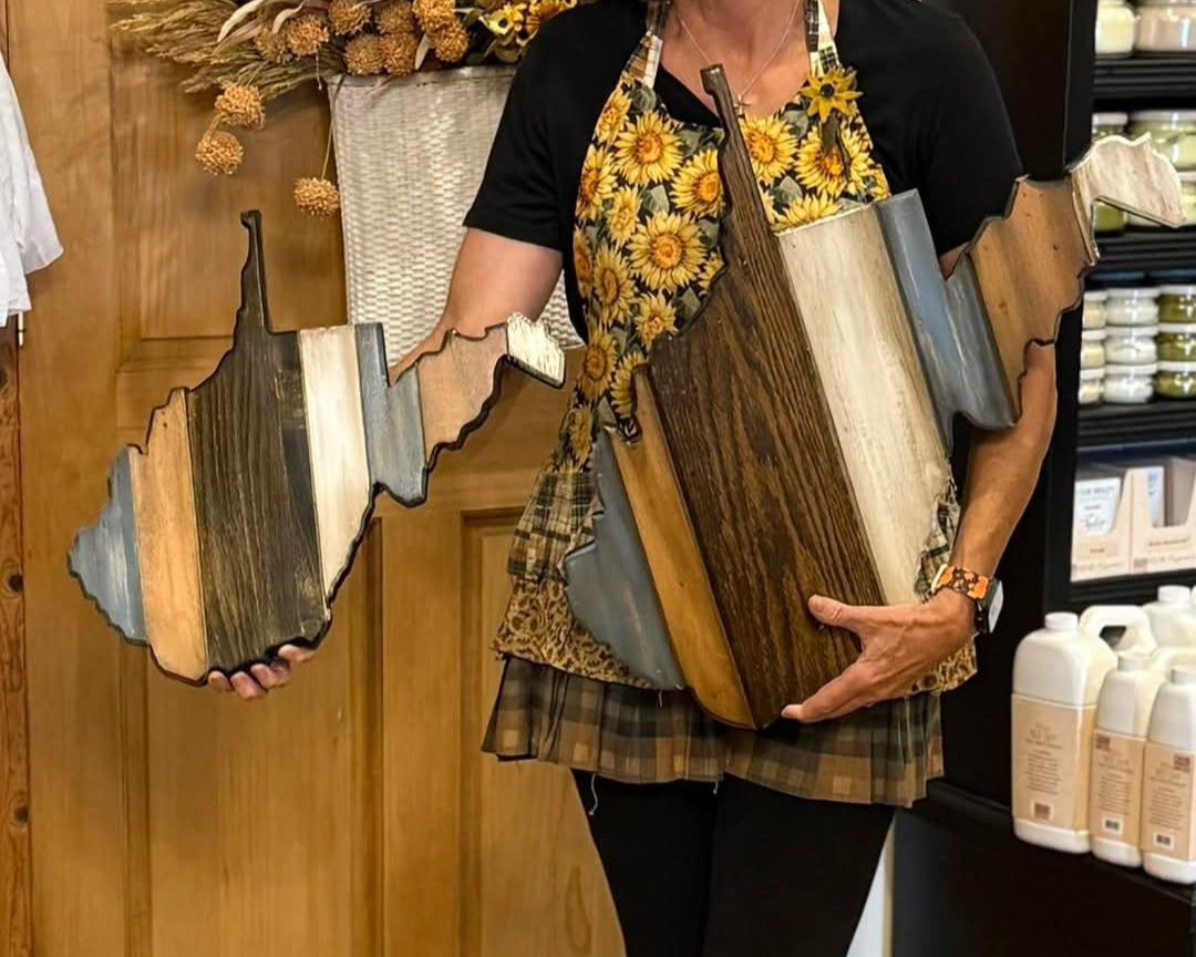 Woman holding 2 different sizes of WV wall art in a store setting