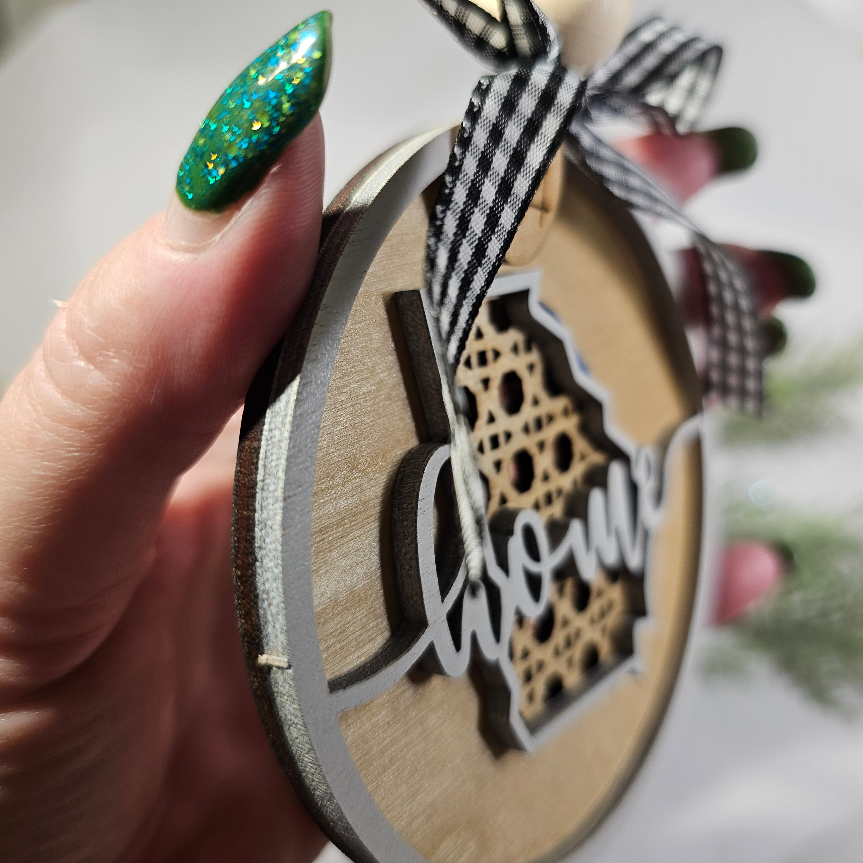 Hand holding a wooden ornament for close up details with a home cutout on a bottom layer of rattan pattern for a vintage vibe.