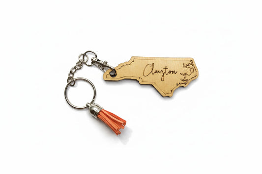 Wooden keychain shaped like a state with 'Clayton' engraving and orange tassel on a white background
