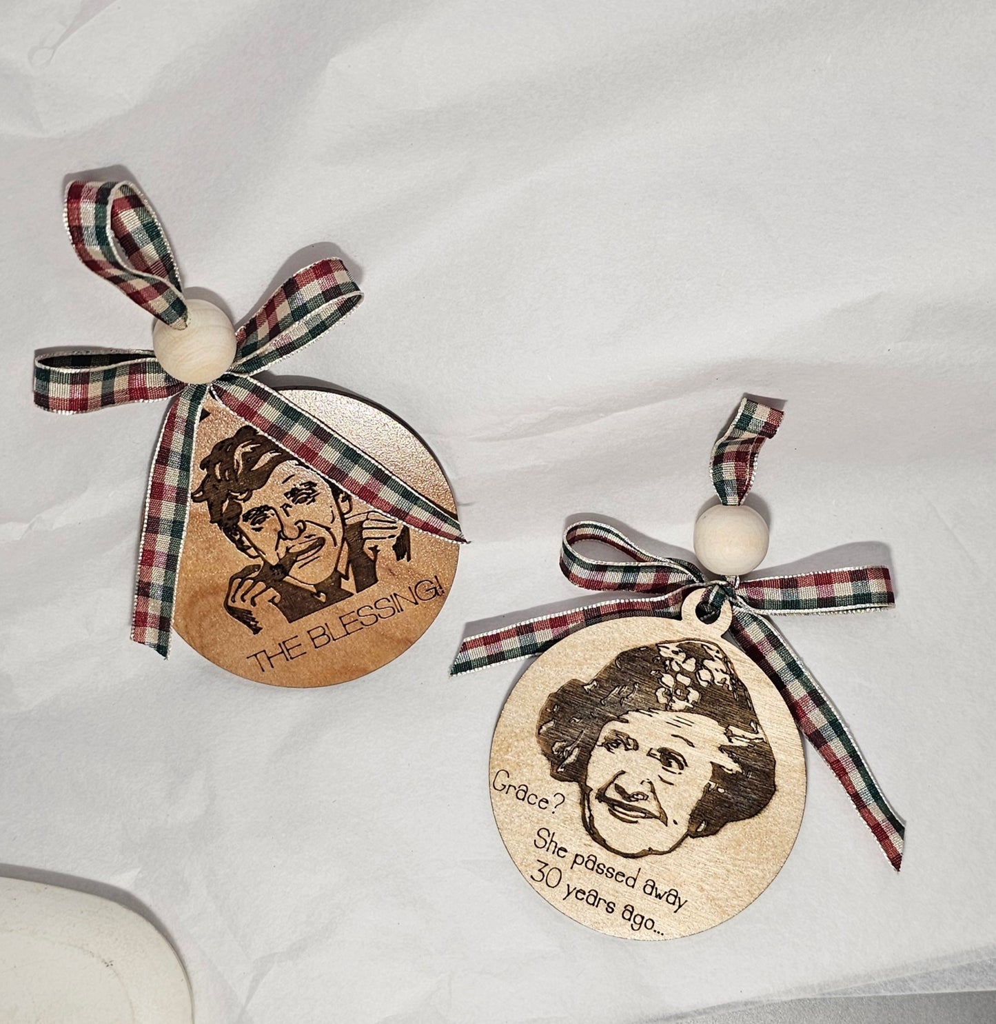 One, double-sided wooden ornament with engraved faces and plaid ribbons on a white background
