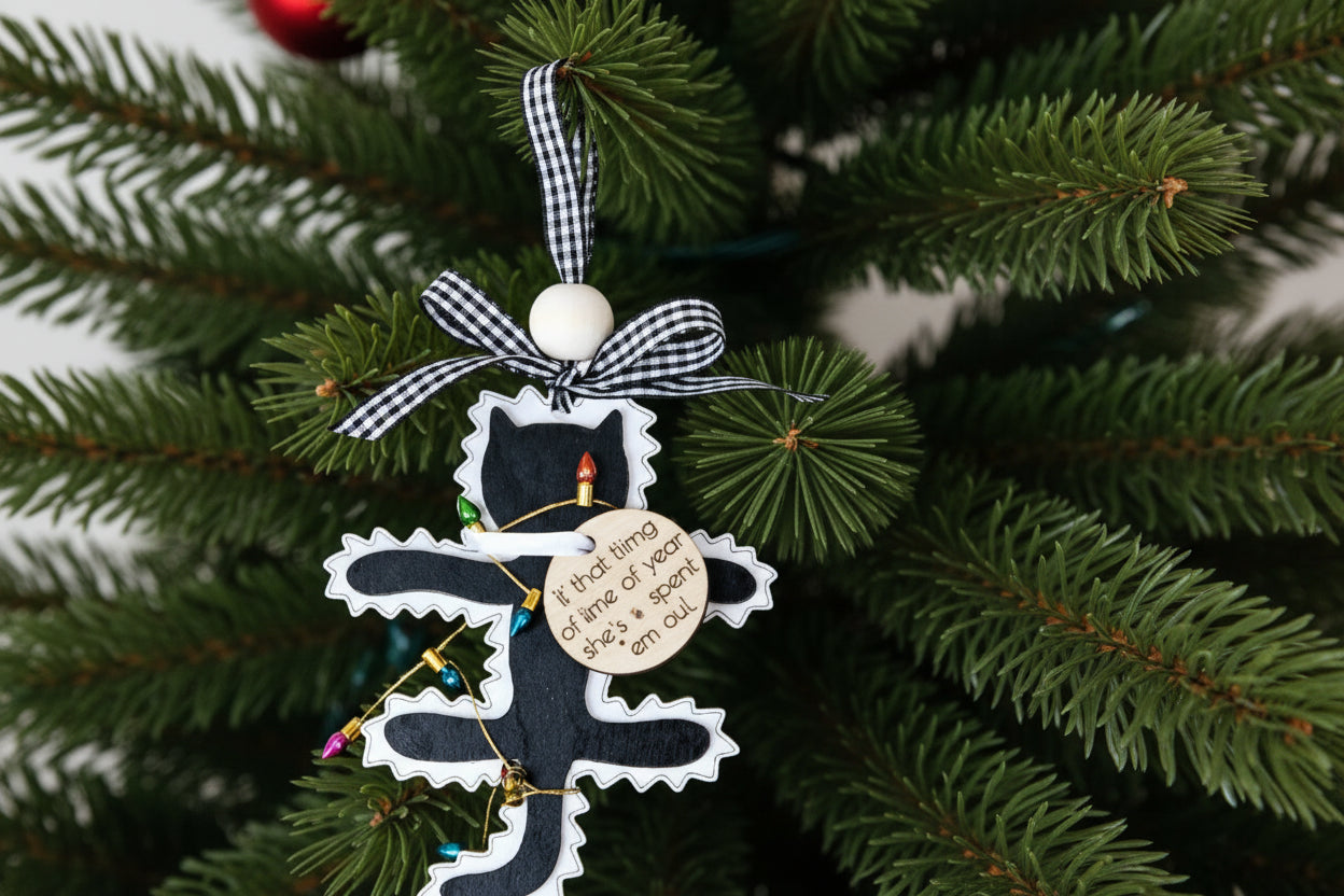 Decorative fried cat Christmas ornament with a black cat design on a branch with pine cones and red ornaments.
