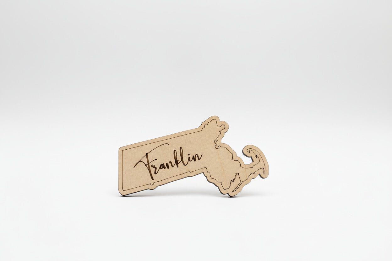 Wooden cutout of the state of Massachusetts magnet with 'Franklin' engraved on it. Rustic state shaped refrigerator magnets, handmade wood keepsakes, farmhouse kitchen decor, vacation souvenir gift idea