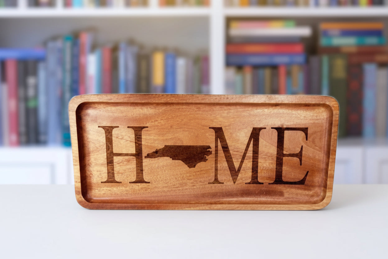Wooden sign with 'HOME' engraved, featuring a state outline, on a wooden surface with a blurred bookshelf background.
