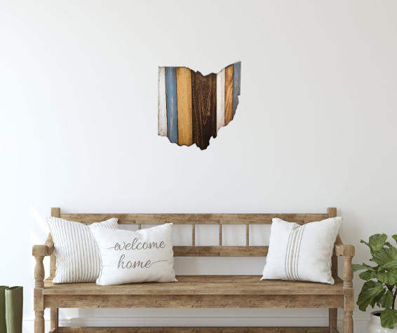 Handmade cut-out in the shape of the state of Ohio hanging over a wood bench with pillows.