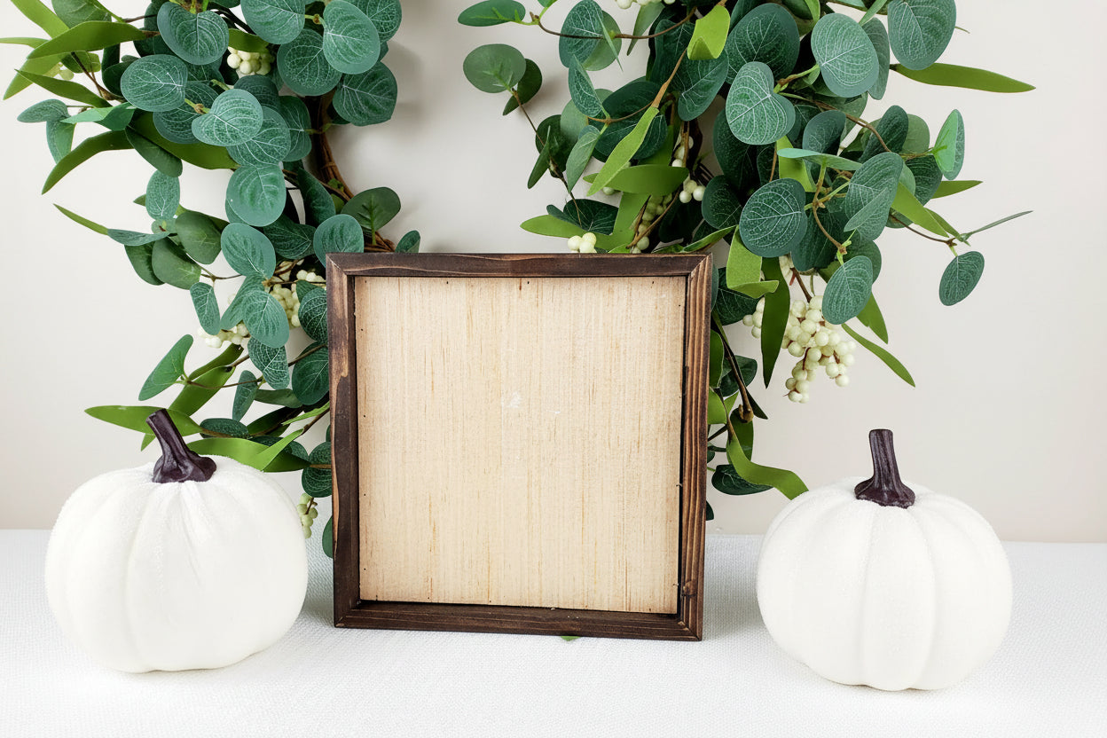 Decorative wreath with green leaves and white berries, featuring the back of a wooden picture frame in the center.