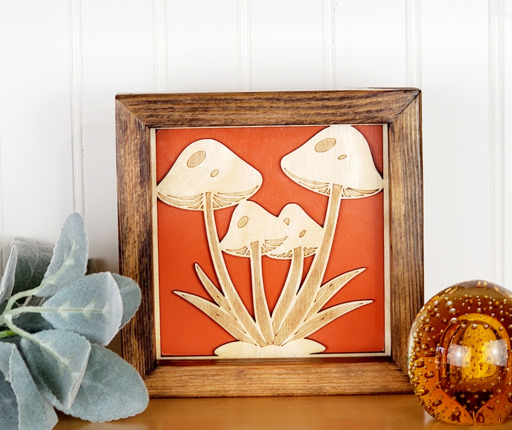 A wooden mushroom-themed wall art with a solid wood frame, featuring engraved mushrooms in a red and orange color scheme.