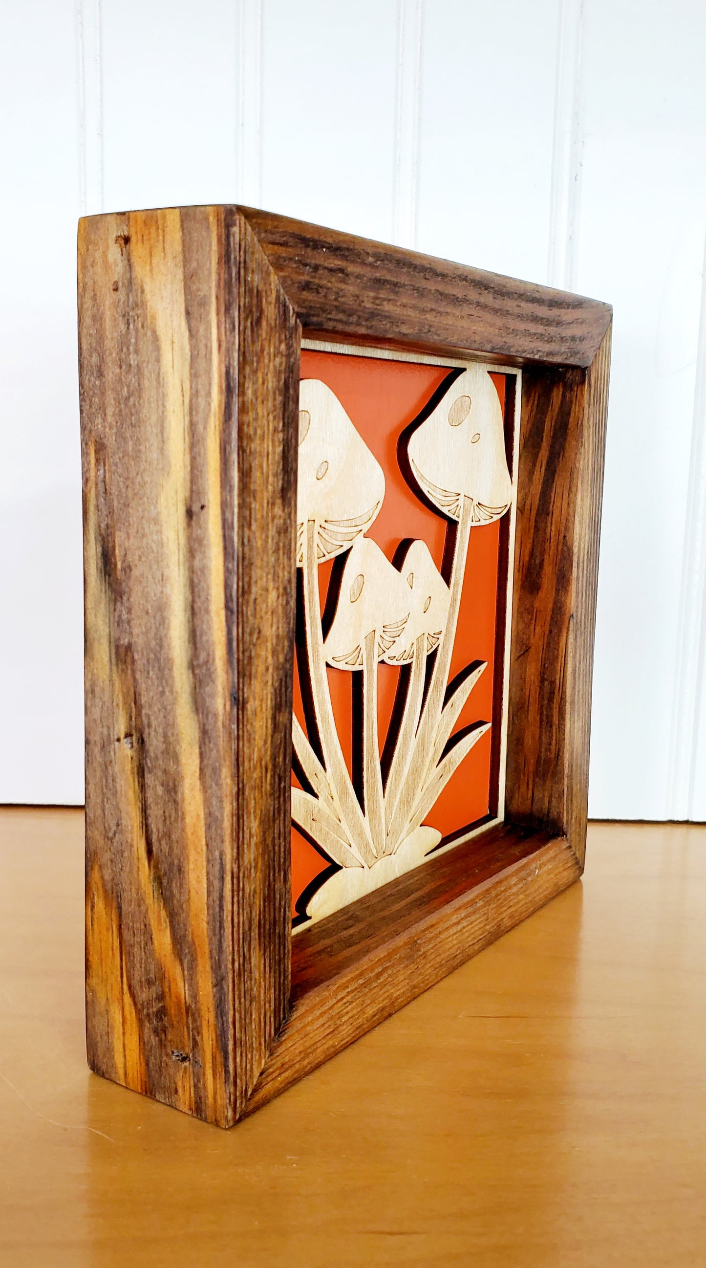 Side view of A wooden mushroom-themed wall art with a solid wood frame, featuring engraved mushrooms in a red and orange color scheme.
